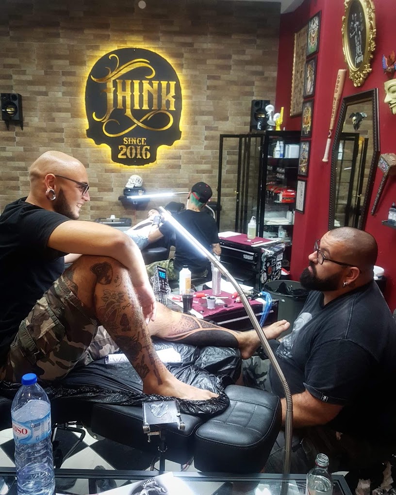 Artista a tatuar um cliente no estúdio ThInk, com o logótipo iluminado ao fundo
